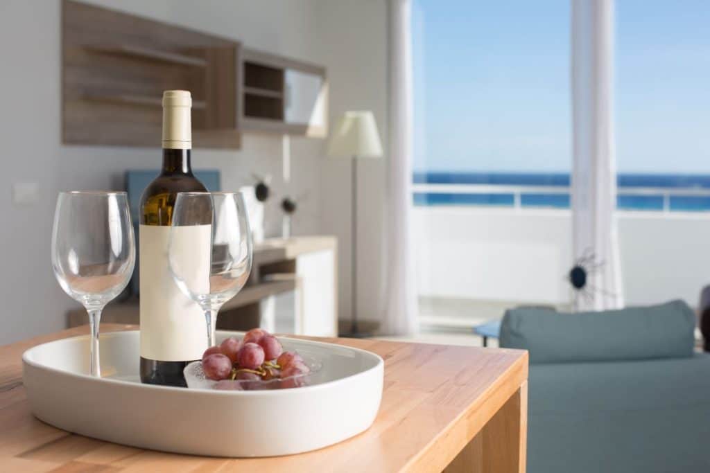 wine bottle and glasses and grapes on tray with ocean views